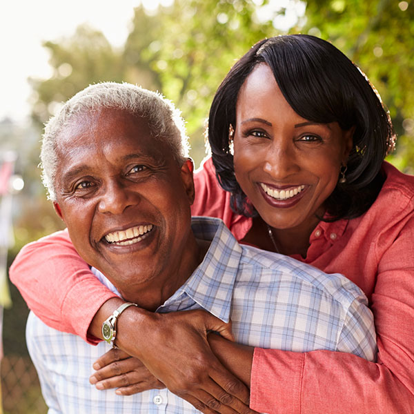 Senior black couple piggyback in garden looking at camera